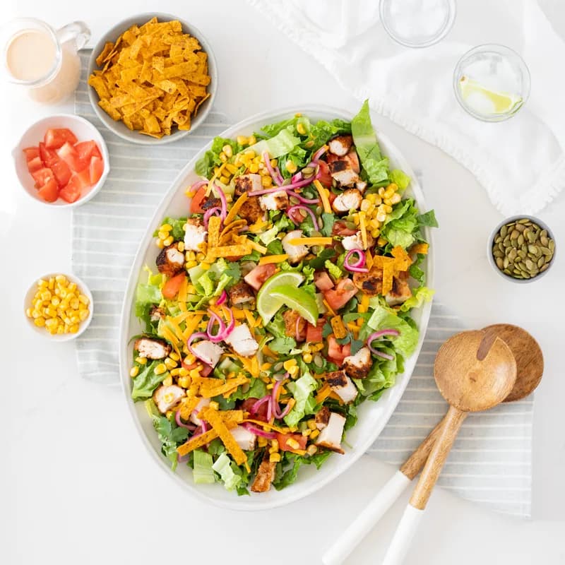 A Southwest salad on an oval platter: chopped romaine, corn, peppers, black beans, red onion and tortilla strips